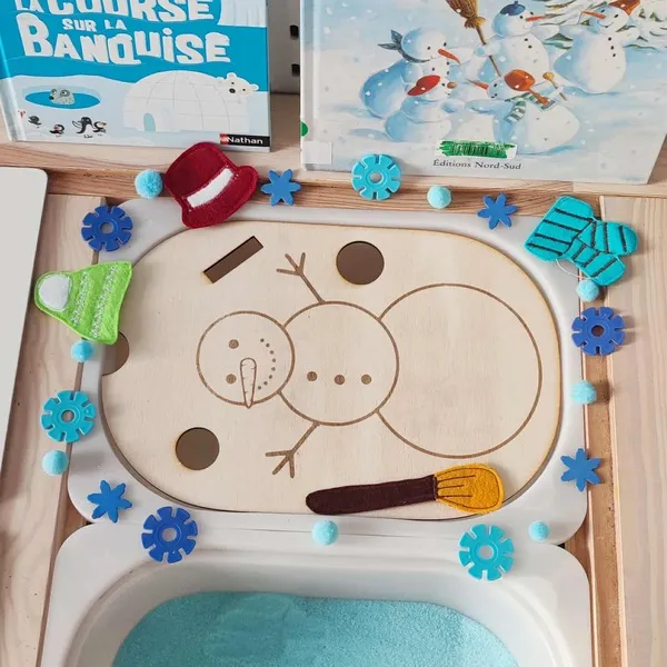 Insert en bois bonhomme de neige décoré d’accessoires en feutrine et éléments sensoriels bleus sur plateau d’activité banquise