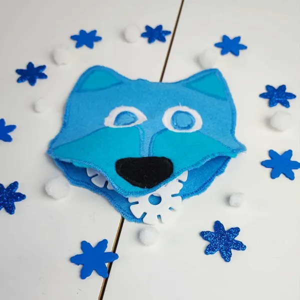 Tête de loup en feutrine bleue avec bouche ouverte contenant un flocon, entourée de décorations bleues et blanches sur fond clair