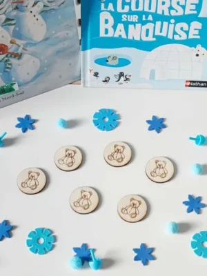 Jetons en bois gravés d’un ourson disposés sur une table décorée d’éléments bleus hivernaux, devant des livres sur la banquise et la neige