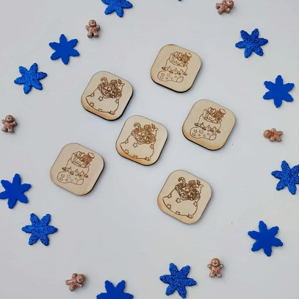 Jetons en bois gravés représentant la hotte du Père Noël remplie de jouets et de friandises, entourés de flocons bleus et de petits personnages en pain d’épice