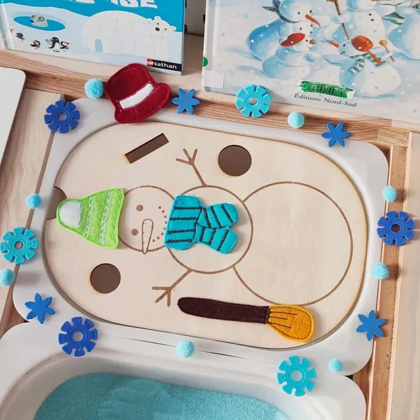 Insert en bois bonhomme de neige décoré de pièces en feutrine colorée et éléments sensoriels bleus sur plateau d’activité hiver