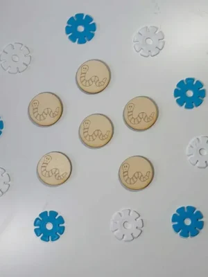 Jetons en bois gravés d’un petit ver souriant, disposés parmi des flocons bleus et blancs pour activité sensorielle Montessori