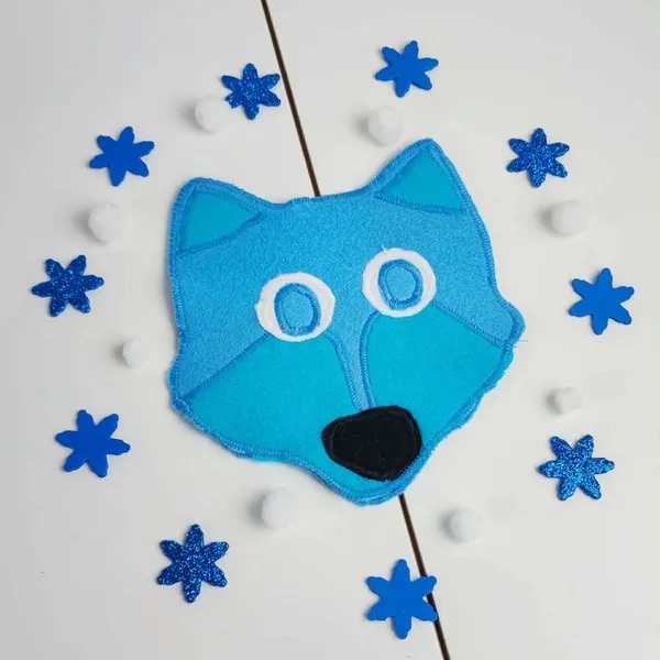 Tête de loup en feutrine bleue cousue main, entourée de flocons scintillants bleus et de boules blanches sur fond clair