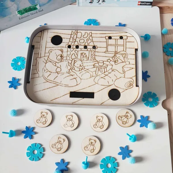 Plateau sensoriel Montessori en bois gravé illustrant des ours polaires lisant au coin du feu, accompagné de jetons oursons et éléments bleus décoratifs