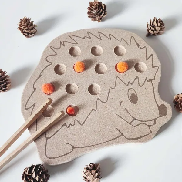 Plateau de motricité fine hérisson en MDF avec trous pour pompons orange, entouré de petites pommes de pin.