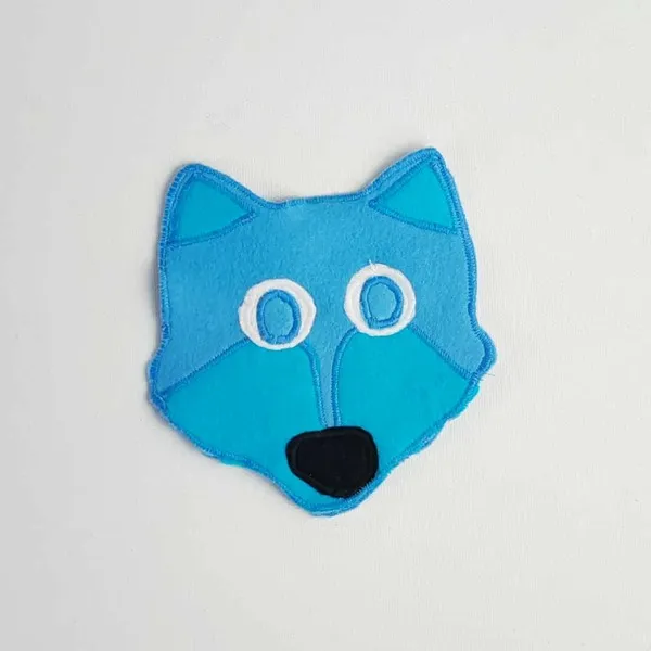 Tête de loup en feutrine bleue et turquoise avec museau noir et yeux blancs, création textile artisanale sur fond clair
