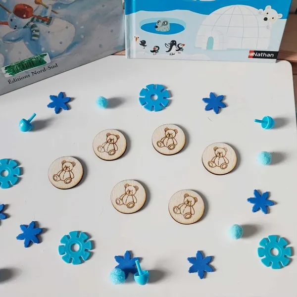 Jetons ronds en bois gravés d’un ourson disposés sur une table blanche décorée d’éléments bleus, inspirés de l’hiver et de la banquise