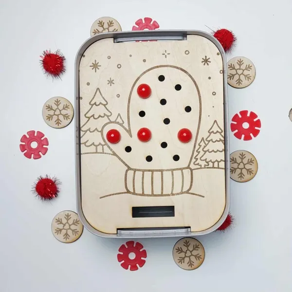 Plateau d’activité en bois gravé représentant une moufle d’hiver avec trous pour pompons, accompagné de jetons flocons en bois.