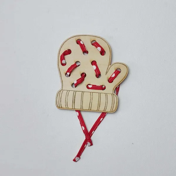 Carte à lacer en bois en forme de moufle, lacée avec un ruban rouge à pois blancs sur fond blanc.