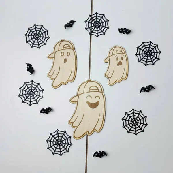 Ensemble de trois fantômes en bois avec casquette, chacun portant une expression différente, entourés de toiles d’araignée noires et de petites chauves-souris décoratives.