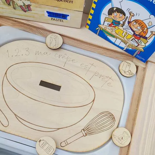 Plateau pédagogique crêpes en bois avec jetons ingrédients et livres jeunesse en arrière-plan