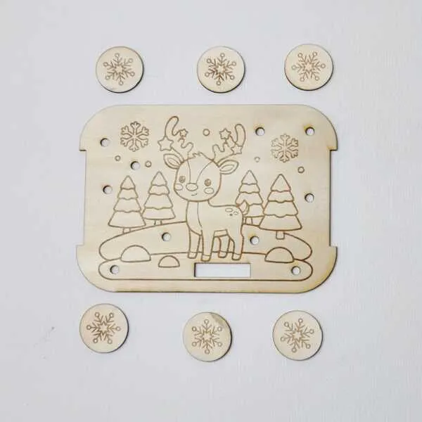 Plaque en bois gravée d’un renne dans un paysage enneigé avec des jetons flocons disposés autour.