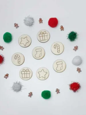 Jetons en bois gravés sur le thème de Noël, entourés de pompons colorés et de mini personnages en pain d’épice.