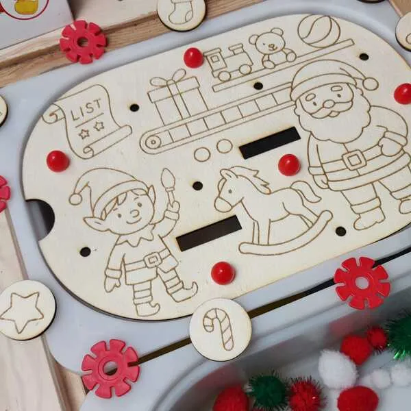 Plateau en bois gravé sur le thème de Noël avec un lutin, un cheval à bascule et des jouets, décoré de jetons et de pompons colorés.