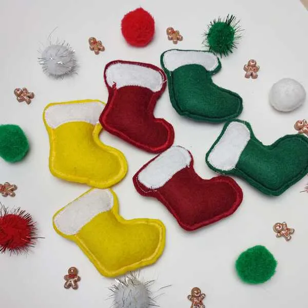 Chaussettes de Noël en feutrine rouge, verte et jaune, entourées de pompons festifs et de petites décorations pain d’épice.