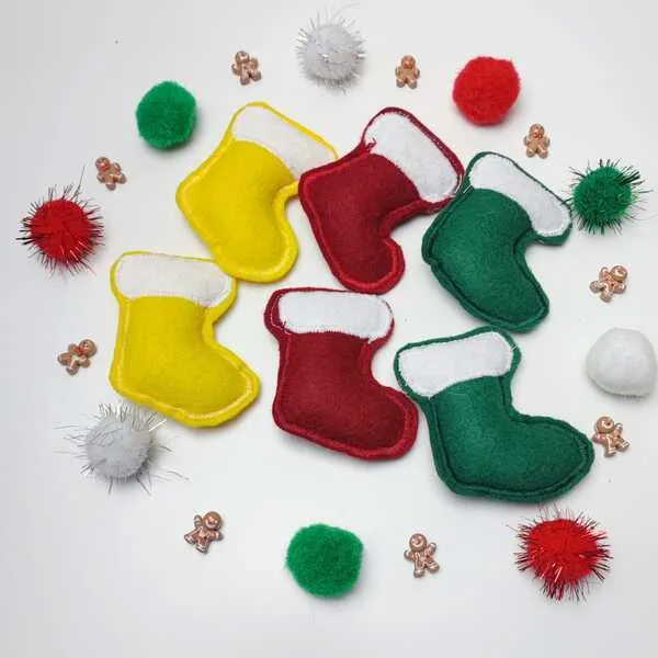 Chaussettes de Noël en feutrine jaune, rouge et verte, entourées de pompons colorés et de petites décorations pain d’épice.