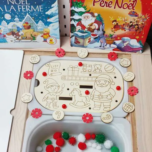 Plateau de motricité fine en bois sur le thème de Noël, représentant un lutin, le Père Noël et des jouets, accompagné de jetons gravés et de pompons rouges, verts et blancs.
