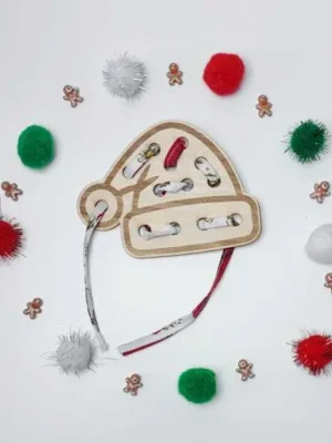 Carte à lacer en bois en forme de bonnet de Noël entourée de pompons festifs et petits bonshommes pain d’épices.