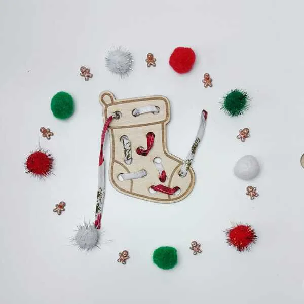 Carte à lacer en forme de chaussette de Noël, entourée de pompons colorés et de petites décorations.