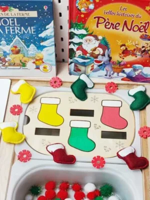 Plateau d’activité de Noël avec des bottes en feutrine colorées à associer aux emplacements en bois, présenté avec des livres et des pompons rouges, blancs et verts.
