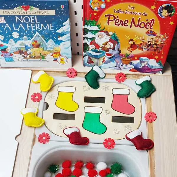 Plateau d’activité de Noël avec des bottes en feutrine colorées à associer aux emplacements en bois, présenté avec des livres et des pompons rouges, blancs et verts.