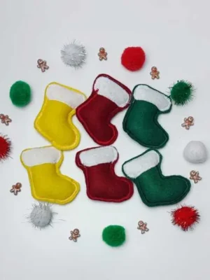 Petites bottes de Noël en feutrine rouge, verte et jaune entourées de pompons colorés et de mini décorations pain d’épice.