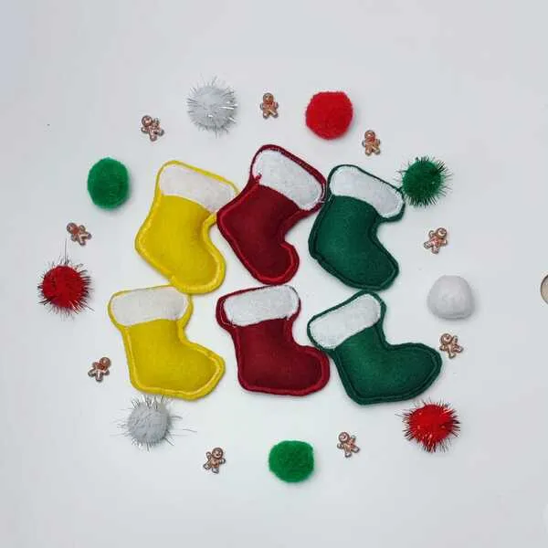 Petites bottes de Noël en feutrine rouge, verte et jaune entourées de pompons colorés et de mini décorations pain d’épice.
