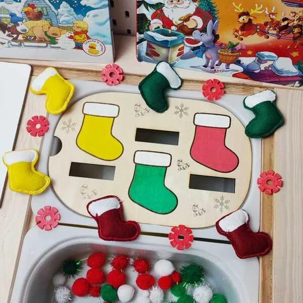 Plateau d’activité de Noël avec chaussettes colorées en bois et chaussettes en feutrine assorties, présenté avec des livres et des pompons festifs.