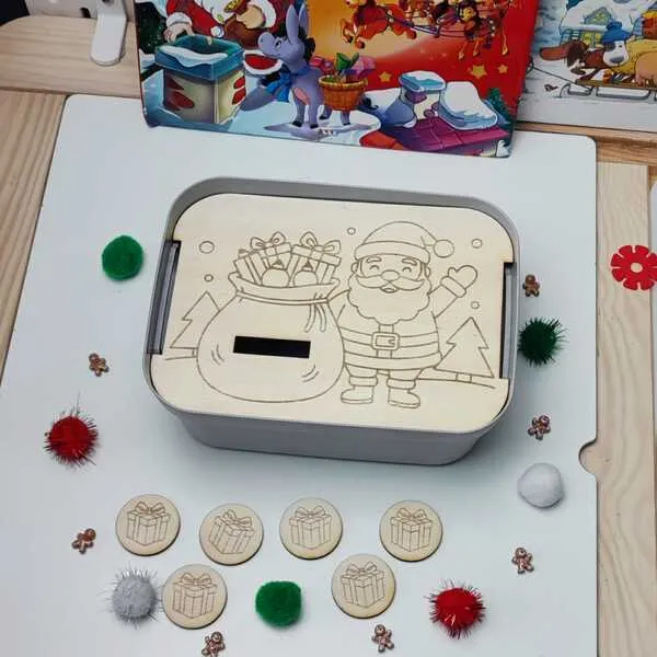 Boîte sensorielle de Noël avec couvercle en bois gravé représentant le Père Noël et un sac de cadeaux, accompagnée de jetons en bois illustrant des présents.