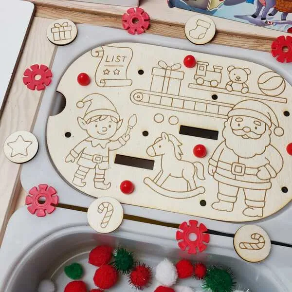 Plateau de motricité fine en bois décoré du Père Noël, d’un lutin et de jouets, accompagné de jetons gravés et de pompons sensoriels rouges, verts et blancs.