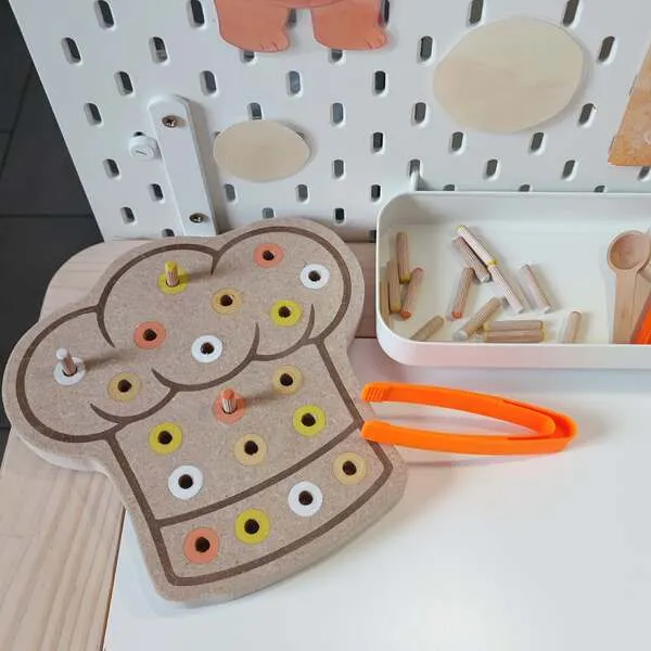 Plateau pic en bois en forme de tablier avec chevilles colorées et pince, activité de motricité fine enfant