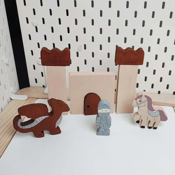 Figurines en bois représentant un chevalier, un dragon et un cheval devant un château