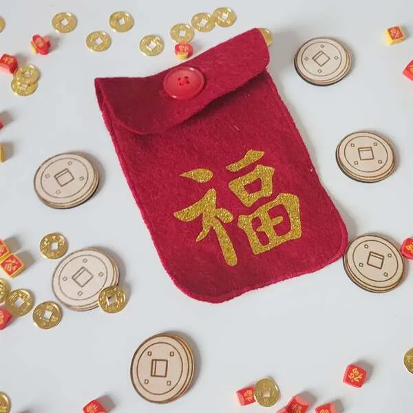 Pochette rouge porte-bonheur en feutrine avec idéogramme chinois doré, entourée de pièces et jetons pour activité sensorielle enfant