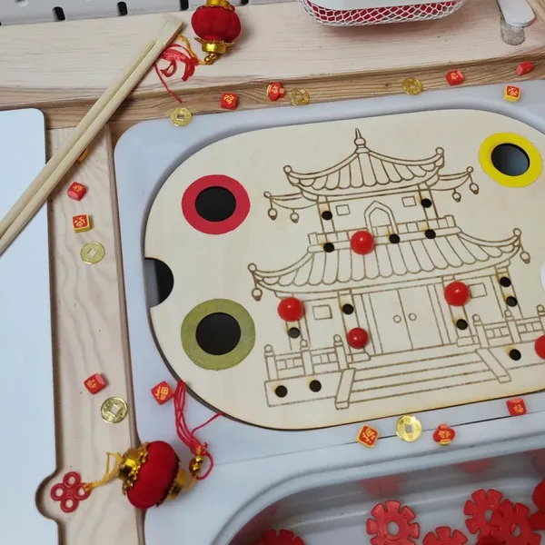 Détail d’un plateau sensoriel en bois sur le thème du Nouvel An chinois avec temple asiatique, jetons rouges et activités de motricité fine
