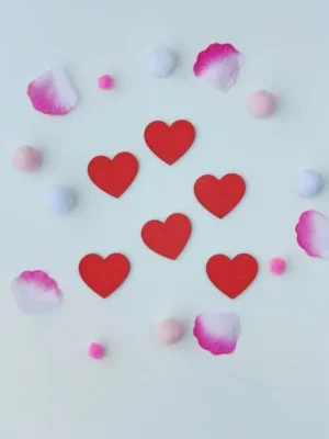 Cœurs rouges en bois disposés sur fond blanc avec pétales et pompons roses pour activité sensorielle enfant