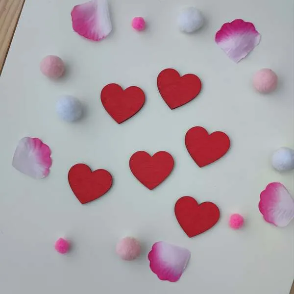 Cœurs rouges en bois entourés de pétales roses et pompons pour activité sensorielle enfant
