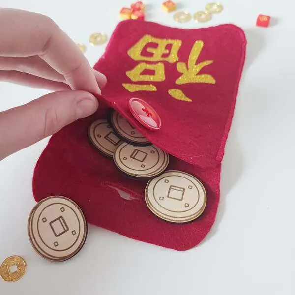 Main d’enfant ouvrant une pochette rouge en feutrine du Nouvel An chinois contenant des pièces en bois pour activité sensorielle