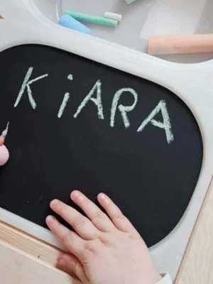 Enfant écrivant le prénom Kiara à la craie sur une ardoise, activité d’écriture ludique