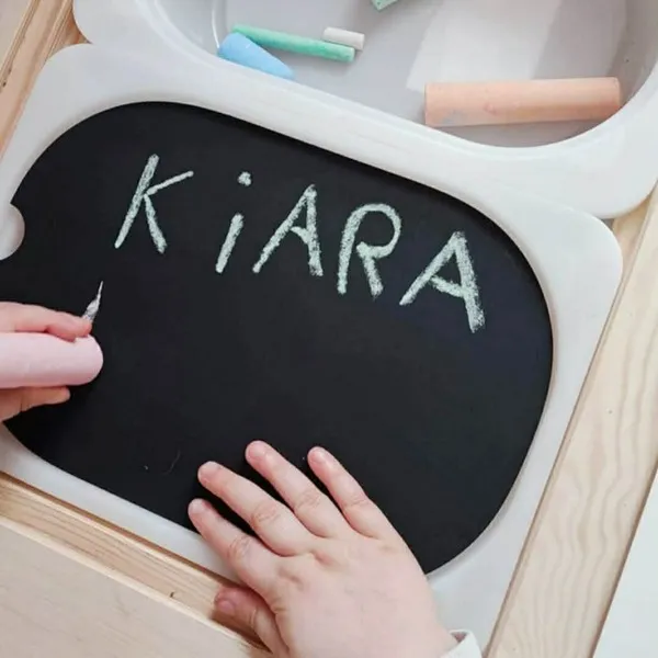 Enfant écrivant le prénom Kiara à la craie sur une ardoise, activité d’écriture ludique