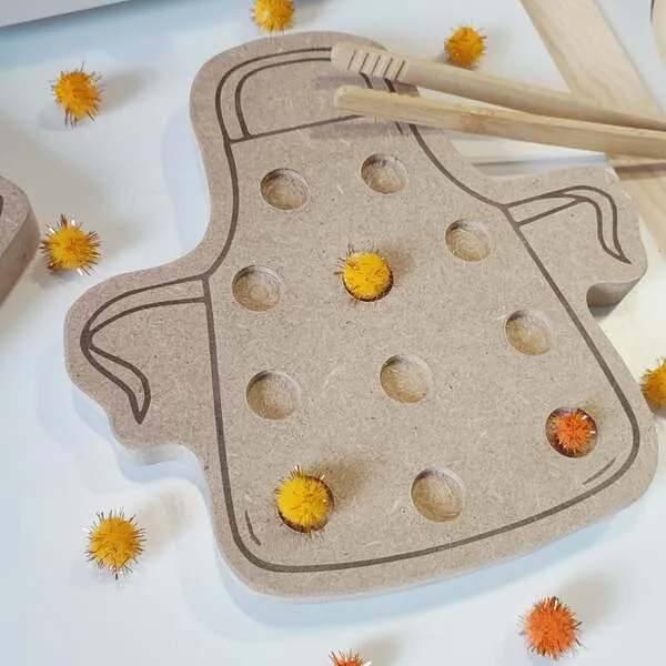 Gros plan d’un plateau de motricité fine en bois en forme de tablier avec pompons à placer
