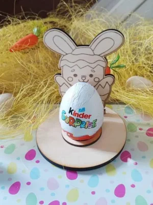 Support en bois thème Pâques avec personnage lapin sortant d’un œuf, tenant un chocolat type œuf surprise, décor paille et carottes.