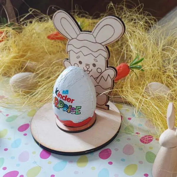 Support en bois thème Pâques avec lapin sortant d’un œuf, tenant un œuf surprise en chocolat, décoré de paille et carottes.