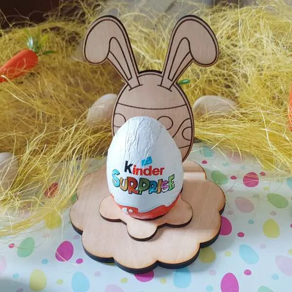 Support en bois pour œuf de Pâques avec silhouette de lapin aux grandes oreilles, posé sur socle fleur et tenant un œuf en chocolat.