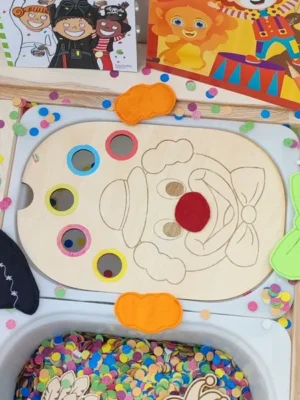 Plateau de motricité fine en bois thème carnaval avec visage de clown et confettis colorés