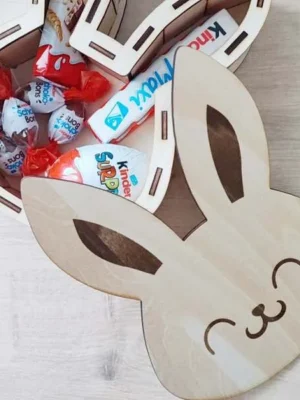 Boîte en bois en forme de tête de lapin ouverte, remplie de chocolats et surprises de Pâques.
