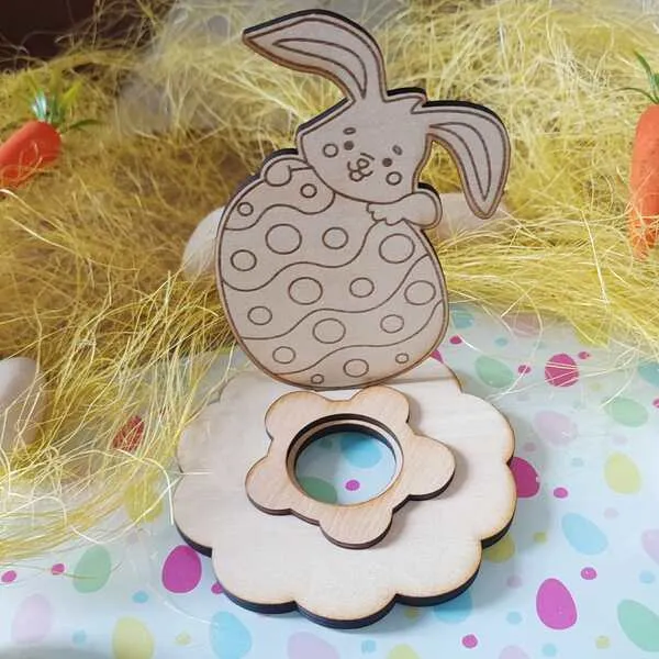 Support en bois pour œuf de Pâques avec lapin tenant un œuf décoré, posé sur un socle en forme de fleur avec emplacement central circulaire.