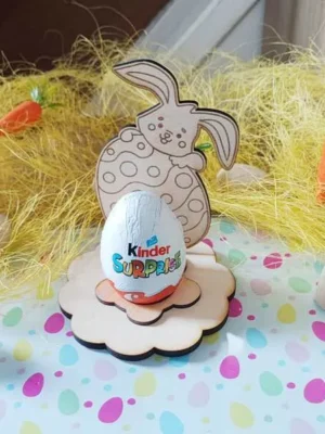 Support œuf de Pâques en bois avec lapin tenant un œuf décoré, socle fleur et œuf en chocolat posé au centre.