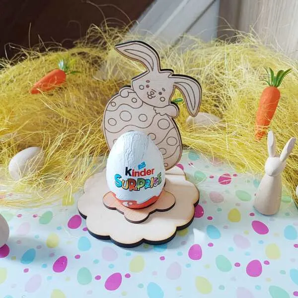 Support œuf de Pâques en bois avec lapin tenant un œuf décoré, socle fleur et œuf en chocolat posé au centre.