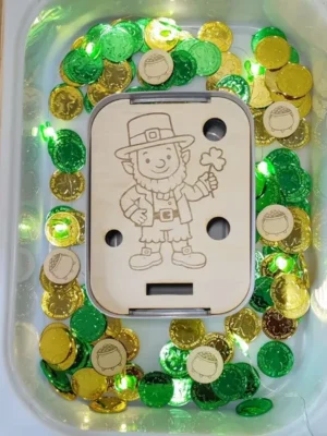 Insert en bois gravé lutin Saint Patrick dans bac sensoriel avec pièces dorées et vertes.