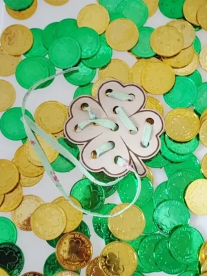 Carte à lacer en bois en forme de trèfle posée sur des pièces d’or vertes et dorées thème Saint Patrick.